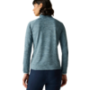 Personne vue de dos portant un pull bleu-vert texturé à manches longues et col montant, et un legging bleu marine, fond beige uni