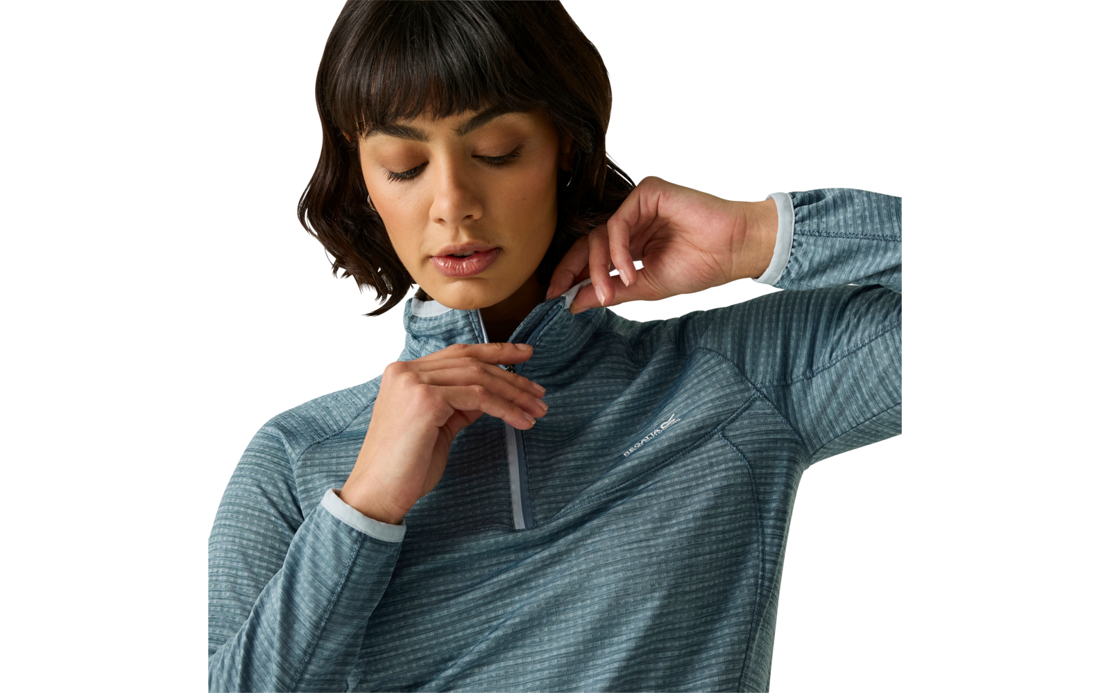 Gros plan d'une femme aux cheveux foncés tirant la petite fermeture éclair d'un haut bleu texturé à manches longues ; fond uni et clair