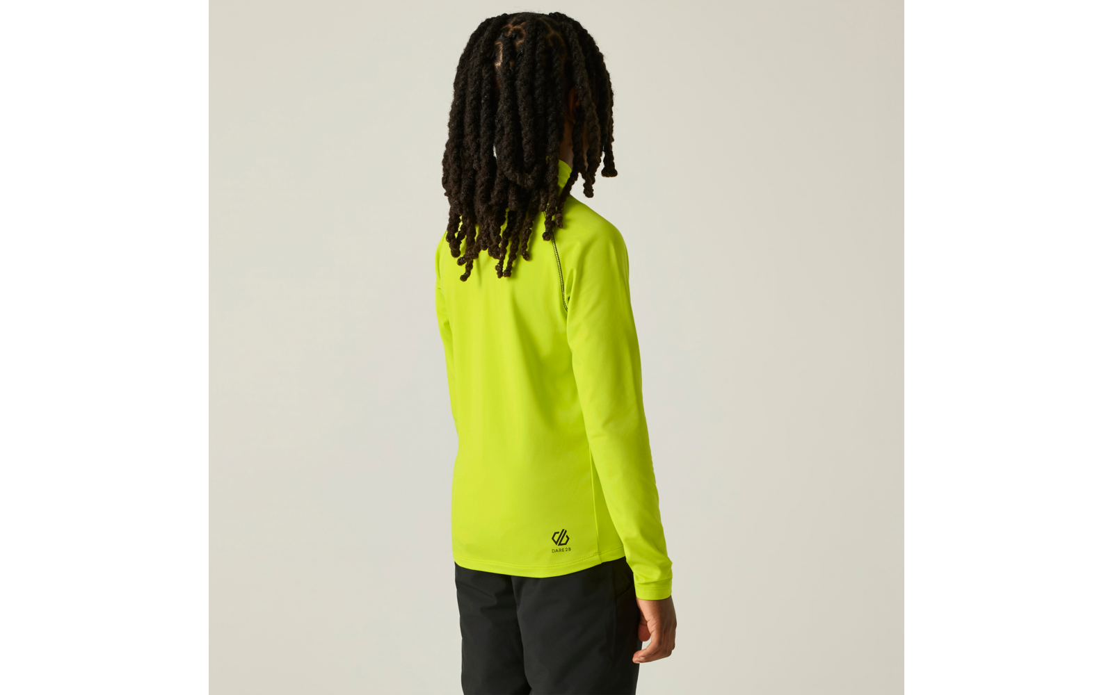 Persoon van achteren met lange dreadlocks, draagt een neon geelgroene longsleeve en zwarte broek voor een lichte achtergrond