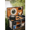 Malle ouverte à intérieur en bois, miroir rond blanc, unité d'alimentation portable avec écran numérique, sèche-cheveux, vasque, flacons de toilette, seau en plastique marqué WC, rive avec eau et plantes en arrière-plan
