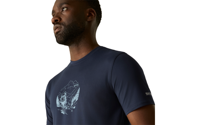 Close-up van het bovenlichaam van een man met een donkerblauw T-shirt met een witte illustratie van bergen en een wandelaar op de borst, beige achtergrond