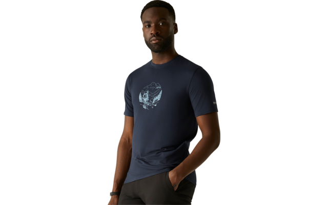 Persoon staat voor een beige achtergrond, draagt een donkerblauw T‑shirt met een lichte cirkelvormige print op de borst, één hand in de zak, kijkt naar de camera