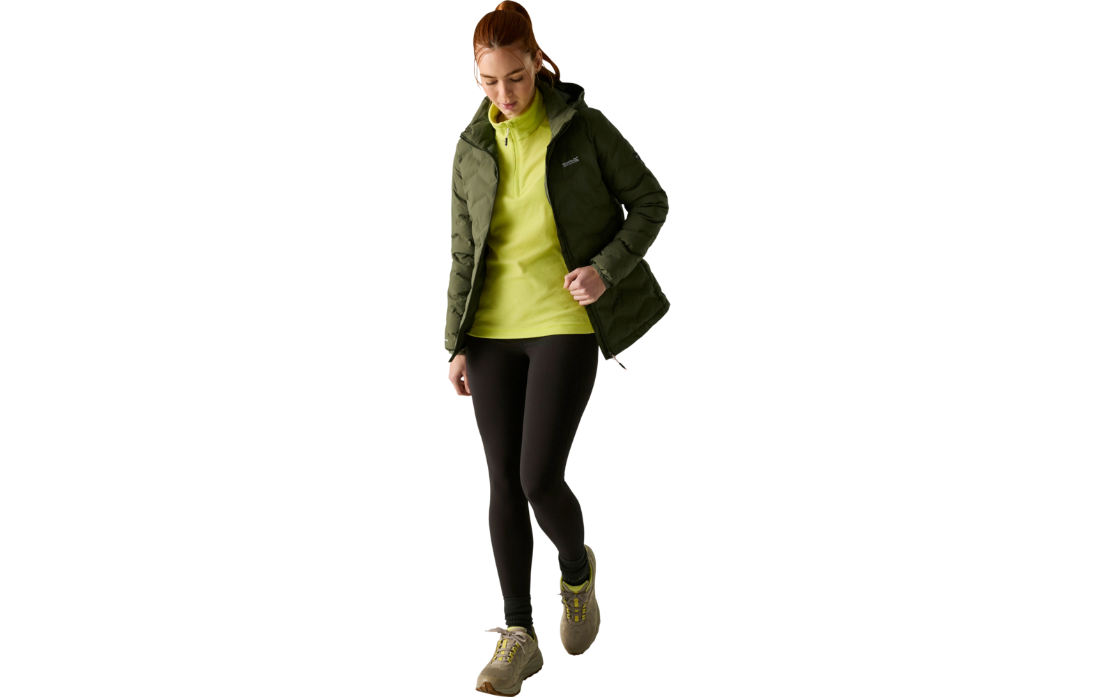 Donna con giacca imbottita verde, felpa con cappuccio verde chiaro, leggings neri e scarpe da ginnastica, guarda verso il basso e cammina su sfondo chiaro