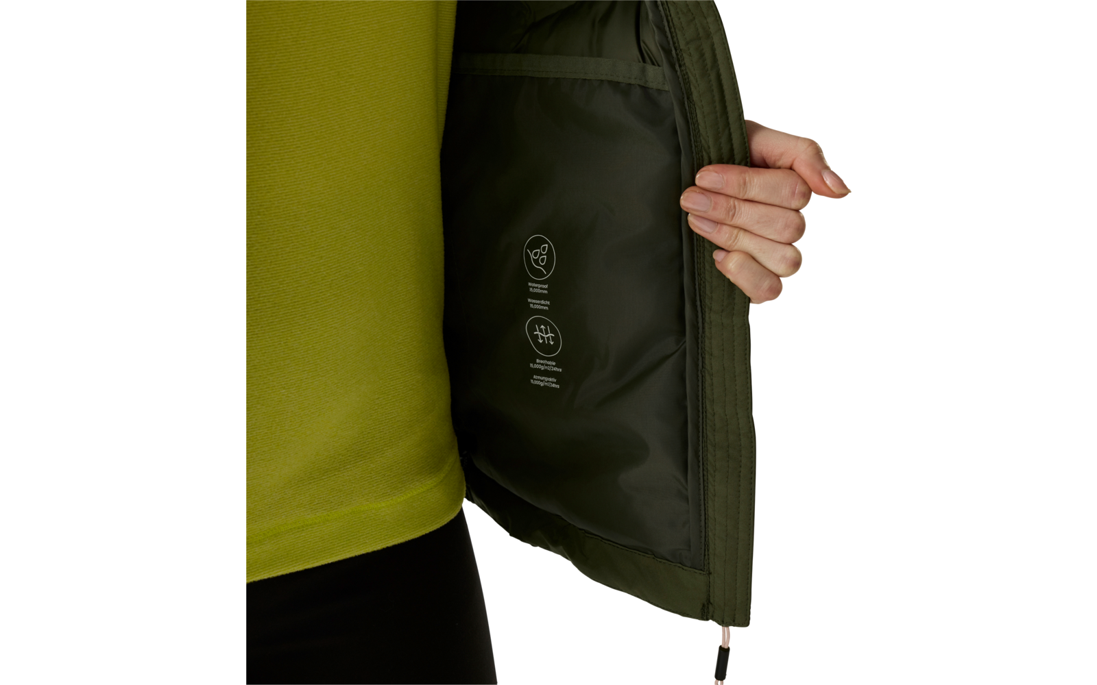 Mano tiene aperta una giacca verde oliva, fodera interna scura con pittogrammi di cura stampati, maglia verde visibile