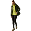 Donna con giacca imbottita verde, felpa con cappuccio verde chiaro, leggings neri e scarpe da ginnastica, guarda verso il basso e cammina su sfondo chiaro