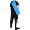 Person von hinten, trägt eine lange blaue zylindrische Tasche über der Schulter, schwarzes T‑Shirt und schwarze Hose mit weißem Streifen