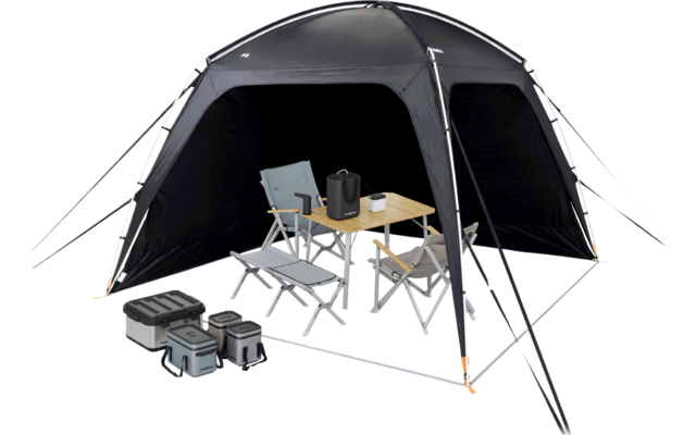 Vrijstaand zwart tent met open ingang; binnenin een opvouwbare houten tafel met een waterkoker en een mok en twee vouwstoelen; links drie opgestapelde boxen; tentstokken en scheerlijnen met oranje punten