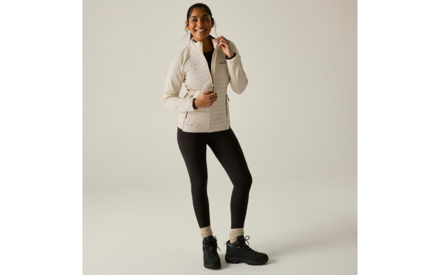 Persona in piedi frontale, indossa una giacca trapuntata chiara, leggings neri, calzini chiari e scarpe da trekking nere, sorridente su sfondo uniforme chiaro