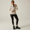 Persona in piedi frontale, indossa una giacca trapuntata chiara, leggings neri, calzini chiari e scarpe da trekking nere, sorridente su sfondo uniforme chiaro