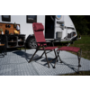 Rode vouwstoel met bijpassende voetensteun op patroonmat voor een geparkeerde caravan met open deur en plank met kookgerei