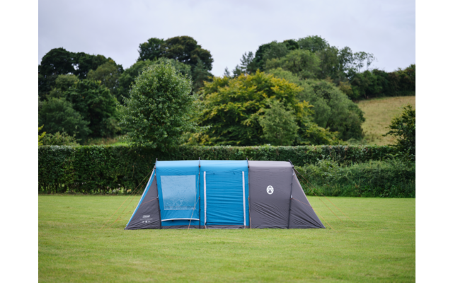 Blau-graues Tunnelzelt auf einer Rasenfläche, dahinter Bäume und bewölkter Himmel