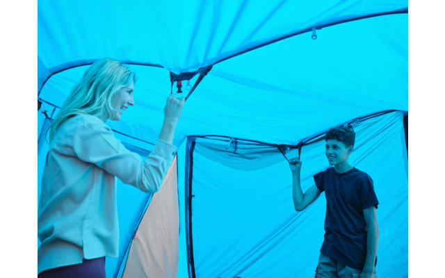 Frau und Junge stehen sich im Inneren eines blauen Zeltes gegenüber und halten das Zeltdach mit den Händen