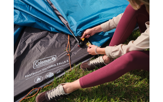 Hände und Beine einer Person befestigen eine Stange am blau-grauen Coleman-Zelt auf Gras