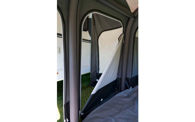 Innenansicht eines aufblasbaren Vorzelts an einem Wohnwagen, geöffnete Stofftür mit Reißverschluss, Matratze rechts, Grasboden sichtbar