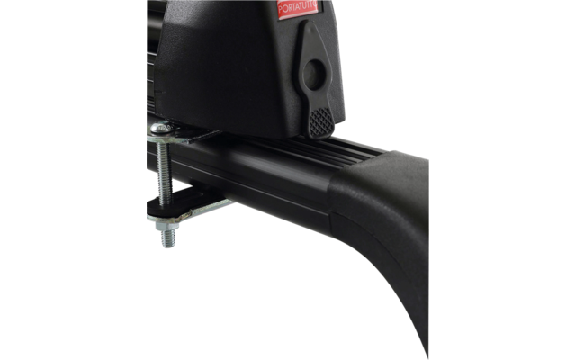 Gros plan d'une traverse de galerie de toit noire avec embout en plastique, pince métallique et boulon visible ; autocollant rouge à inscription blanche ; toit de voiture en arrière-plan