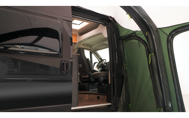 Zwart voertuig met open schuifdeur, zicht op het interieur met bestuurdersstoel, stuur, houten vloer, bovenkast, groen voortent bij de deuropening en dakraam