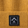 Gorro de punto acanalado color mostaza con vuelta y parche cuadrado negro con un motivo de montaña blanco y el texto 'DARE 2B'