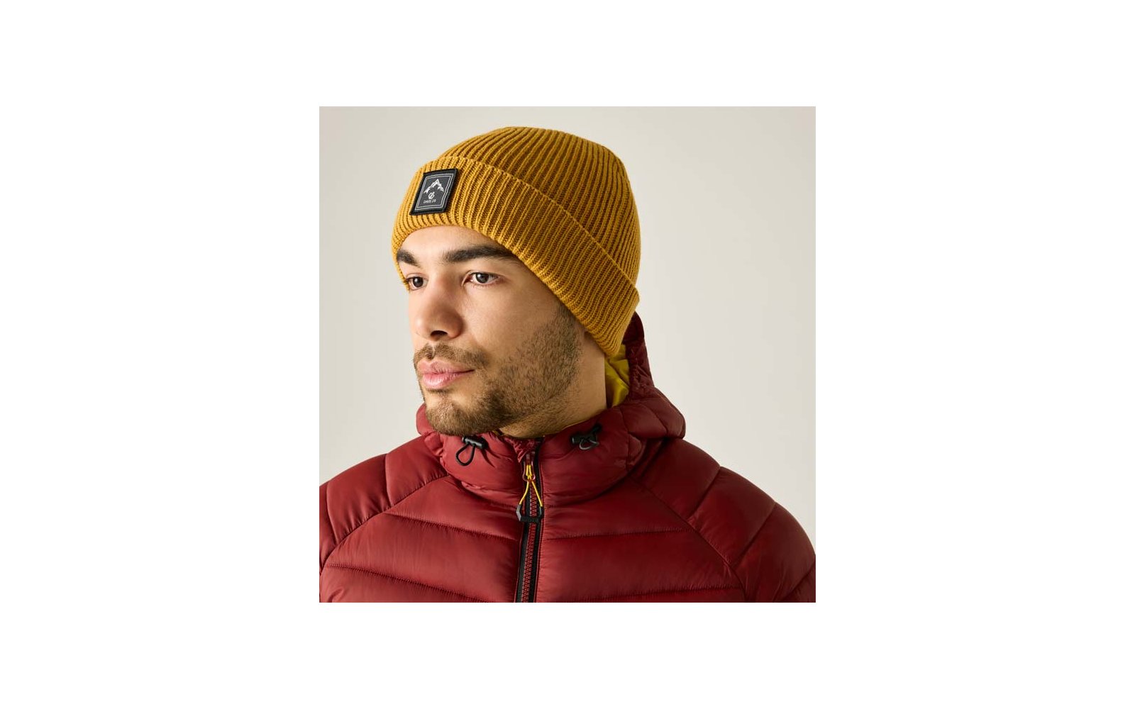 Persona con gorro de punto amarillo y chaqueta acolchada roja, barba corta, mirada hacia la izquierda