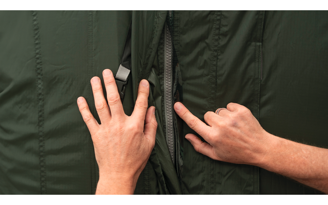 Twee handen die de rits van een donkergroene jas openen, met zichtbare rits en voering
