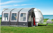 Een wit en grijs tent op groen gras met uitzicht op een meer en blauwe lucht