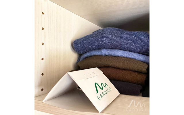 Vier gefaltete Pullover in Blau, Braun und Schwarz auf einem hellen Holzregal