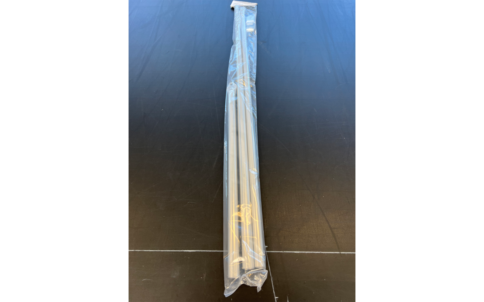 Drei lange, dünne Metallstäbe in einer transparenten Plastiktüte auf einer schwarzen Oberfläche