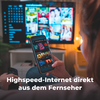 Unscharfe Person von hinten hält Smartphone mit Raster von Film- und Serienvorschaubildern; großer Fernseher im Hintergrund zeigt ebenfalls Vorschaubilder; Fernbedienung in der anderen Hand; weiße Textzeile unten: 'Highspeed-Internet direkt aus dem F