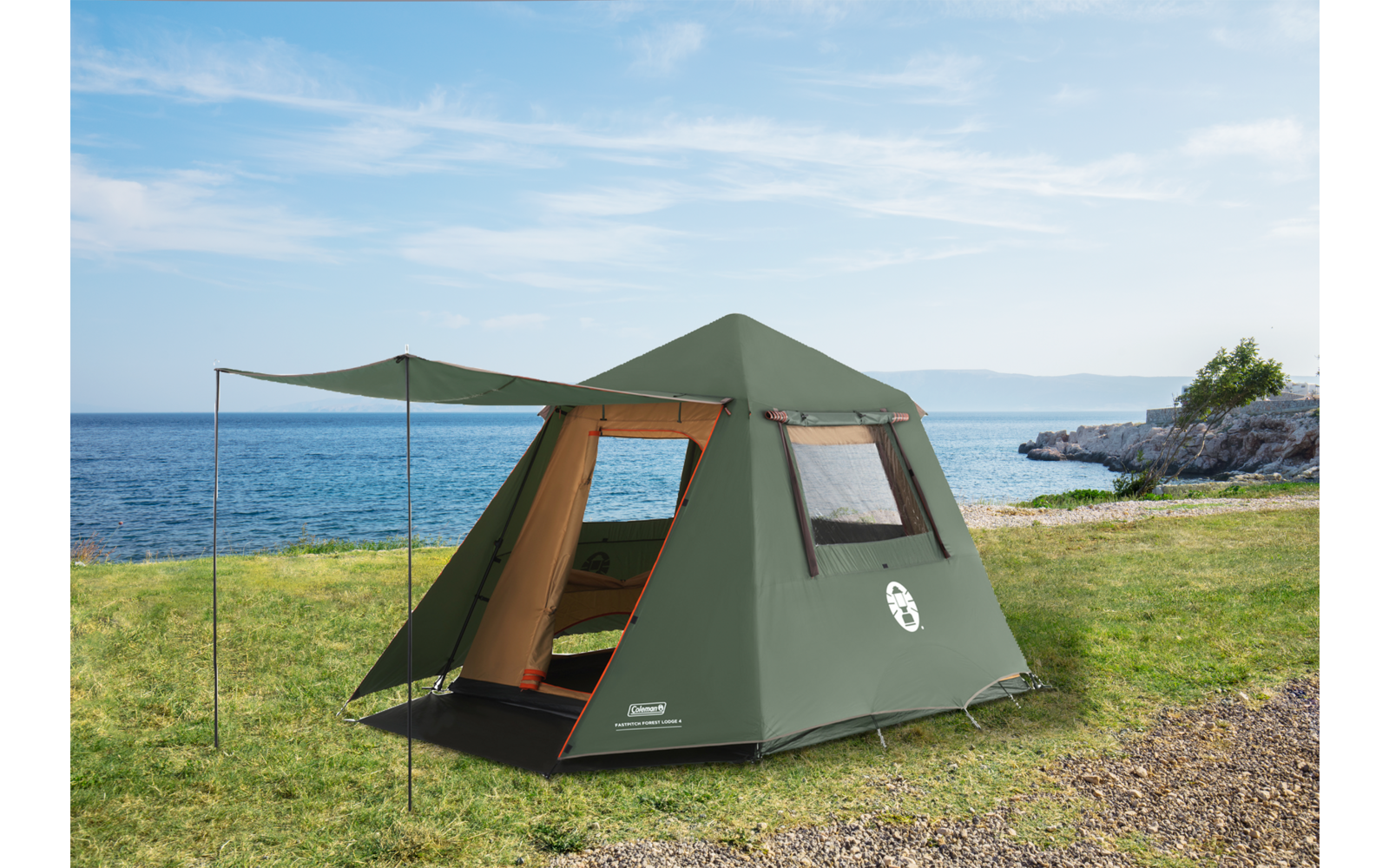 Tenda da campeggio verde con ingresso aperto e tettoia su prato; mare sullo sfondo, scogli a destra, cielo blu con nuvole