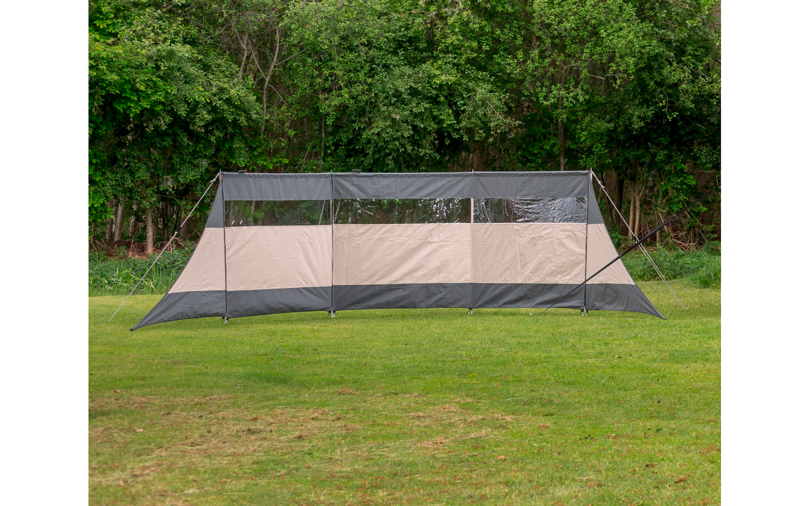 Large rectangular beige and gray tent on a grassy field with trees in the background
