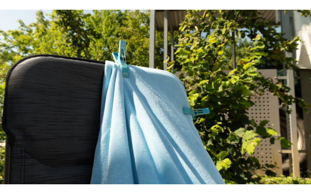 Blauer Mund-Nasen-Schutz hängt an einem schwarzen Koffergriff im Freien