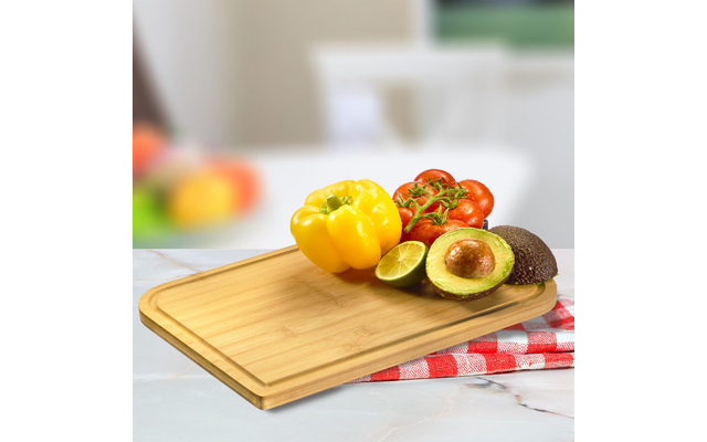 Wooden cutting board with yellow bell pepper, vine tomatoes, halved avocado with pit, lime, and red checkered cloth
