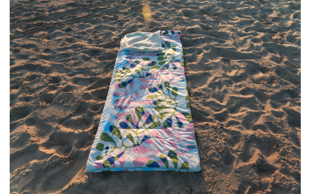 Tapis rectangulaire coloré à motif de feuilles posé sur du sable; sable avec empreintes et ombres