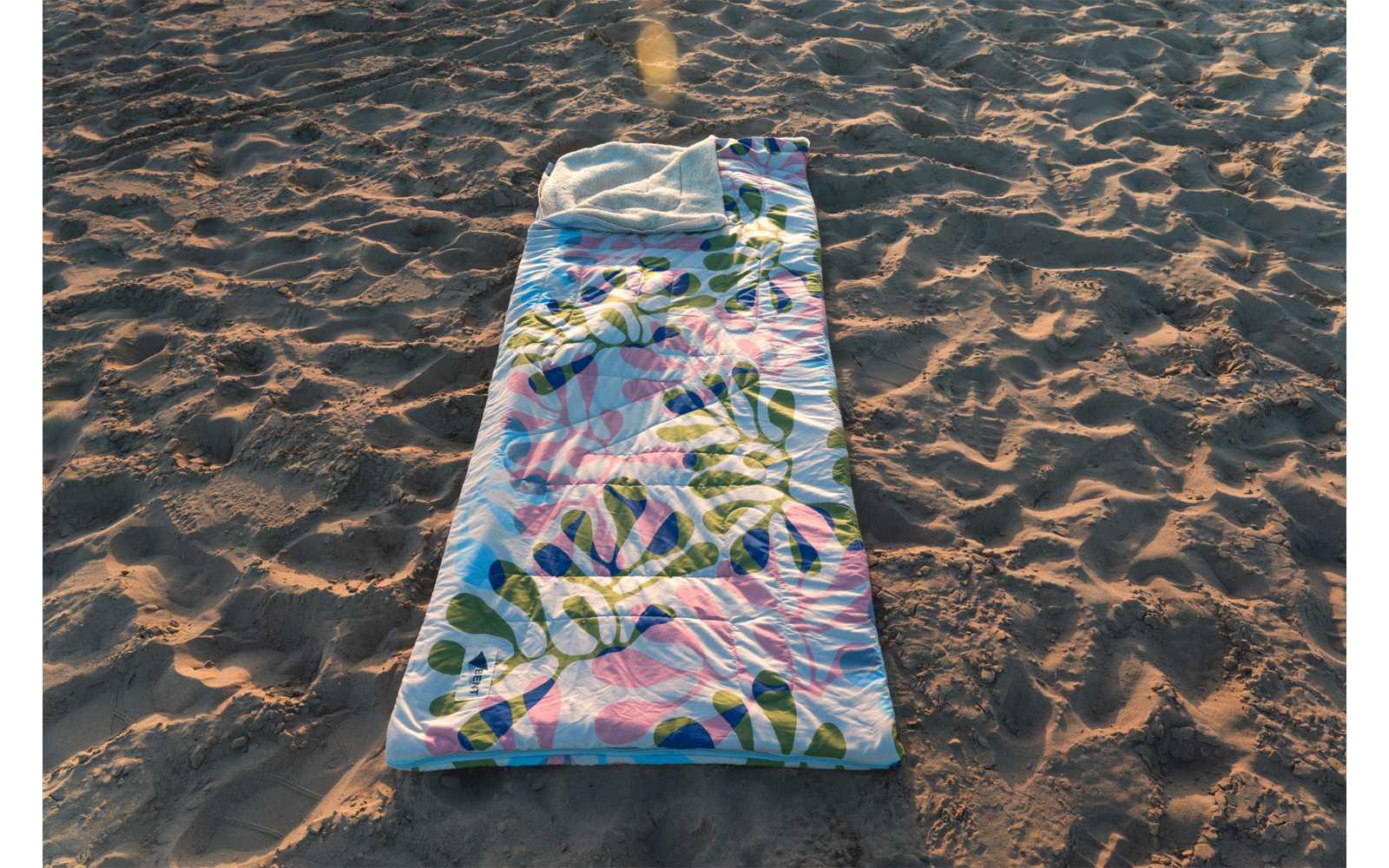 Tapis rectangulaire coloré à motif de feuilles posé sur du sable; sable avec empreintes et ombres