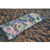 Couverture rectangulaire matelassée avec motif de feuilles vertes et cercles roses posée sur du sable