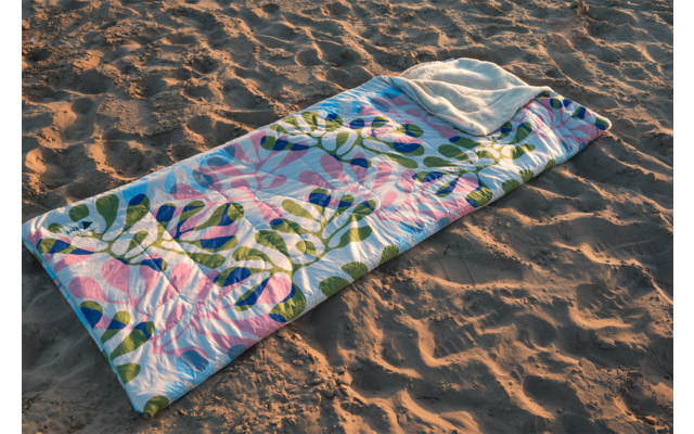 Couverture rectangulaire matelassée avec motif de feuilles vertes et cercles roses posée sur du sable