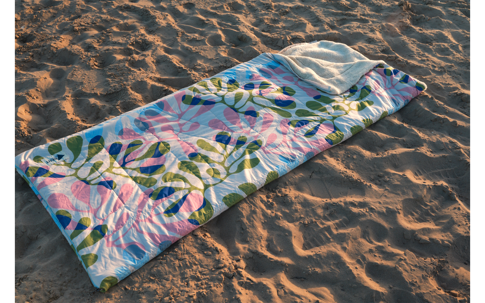 Couverture rectangulaire matelassée avec motif de feuilles vertes et cercles roses posée sur du sable