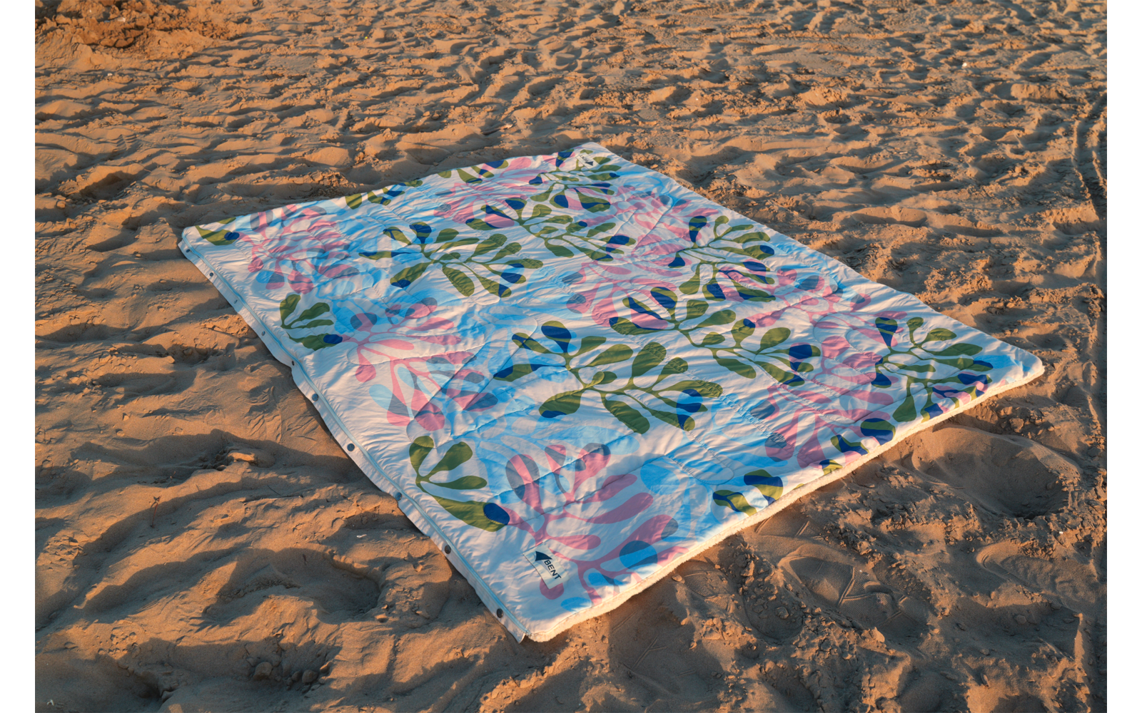 Serviette de plage rectangulaire à motif de feuilles bleu et rose posée à plat sur du sable