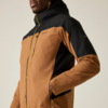Gros plan sur le torse d'une personne portant une veste à capuche marron et noire avec fermetures éclair jaunes, main droite dans la poche, partie inférieure du visage visible