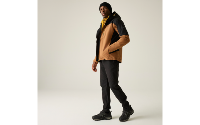 Personne portant une veste brun-noir avec intérieur de capuche jaune, bonnet noir, pantalon noir et chaussures noires, debout une main dans la poche de la veste sur fond clair