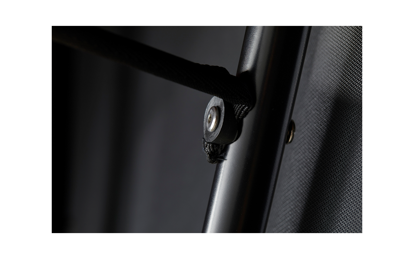 Nahaufnahme eines schwarzen Metallrohrs mit befestigtem schwarzem Gurt, Schraube und Unterlegscheibe, schwarzer Stoff im Hintergrund