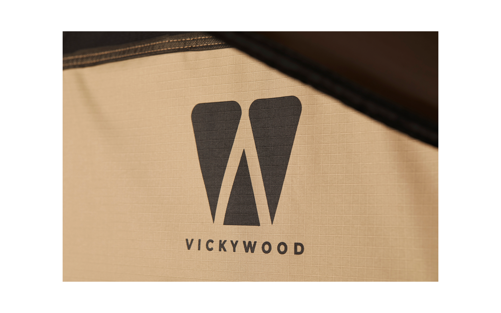 Schwarzes, stilisiertes "W" über dem Schriftzug "VICKYWOOD" auf beigem Stoff