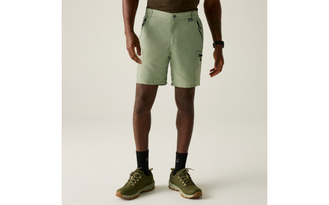 Person von der Hüfte bis zu den Füßen, trägt hellgrüne Shorts mit seitlichen Reißverschlusstaschen, schwarze Socken und olivgrüne Sportschuhe; Hände neben dem Körper