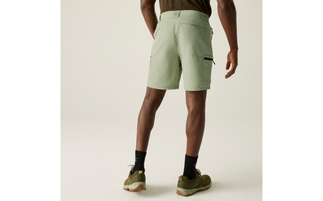 Personne de dos portant un short vert pâle aux genoux, chaussettes noires et baskets vert olive, fond clair