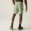 Personne de dos portant un short vert pâle aux genoux, chaussettes noires et baskets vert olive, fond clair