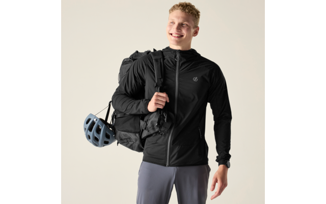 Lächelnde Person mit schwarzer Sportjacke und Rucksack; Fahrradhelm am Rucksack; Blick nach oben rechts