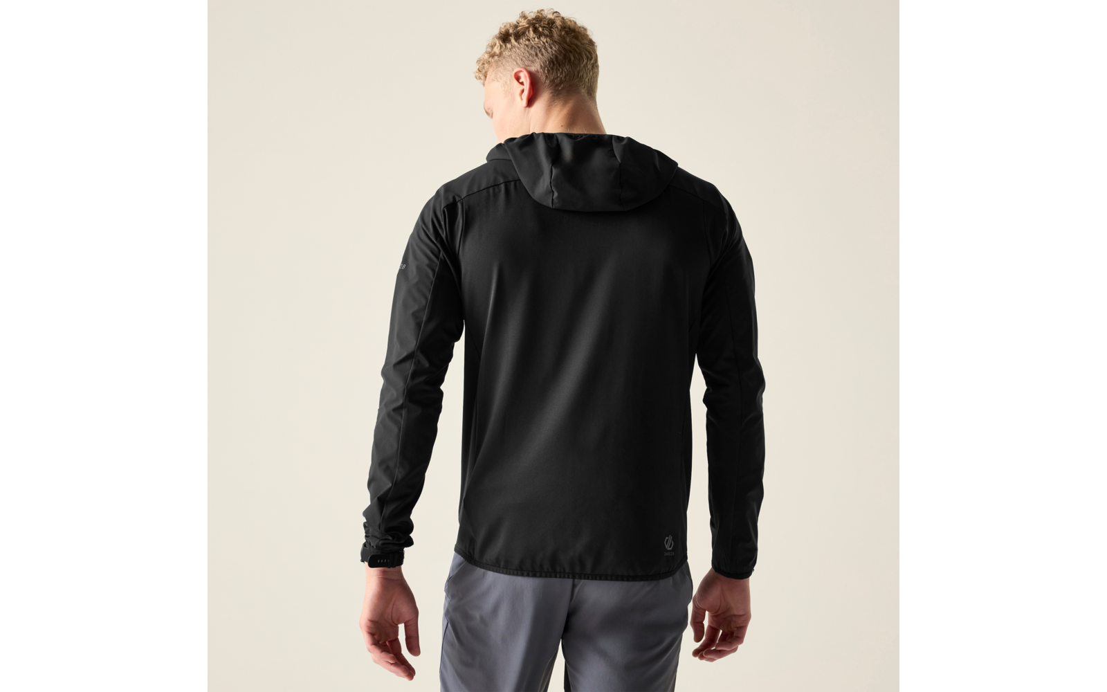 Person von hinten, trägt schwarze Kapuzenjacke und graue Hose vor hellem einfarbigem Hintergrund