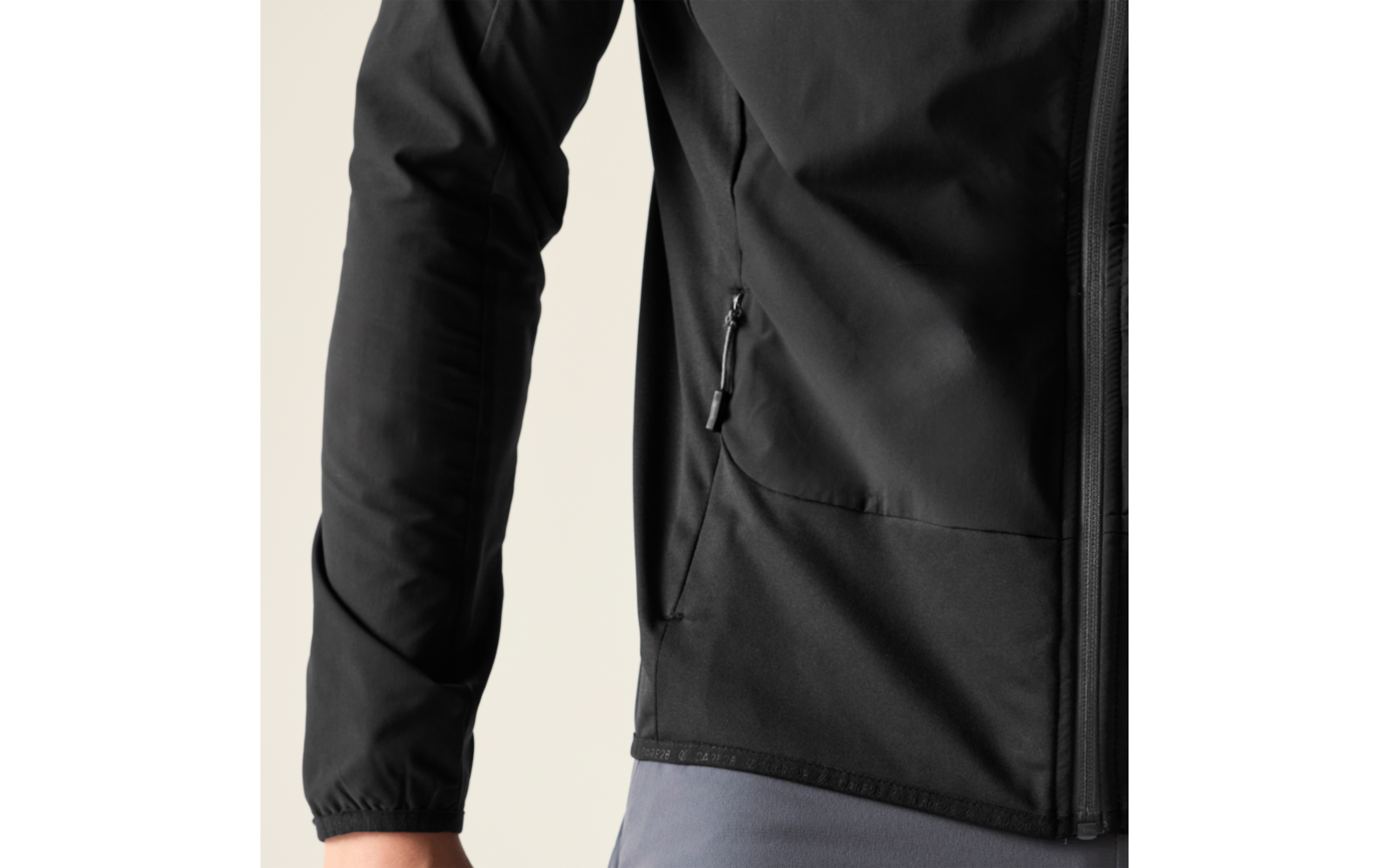 Teilansicht eines Oberkörpers in schwarzer Reißverschlussjacke mit Seitentasche, sichtbare linke Ärmelpartie, graue Hose