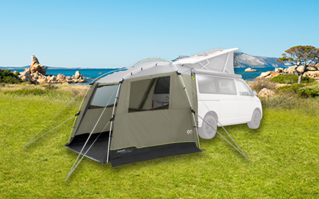 Ein weißes Fahrzeug mit angebautem grauen Zelt auf einer grünen Wiese mit Meer und Felsen im Hintergrund