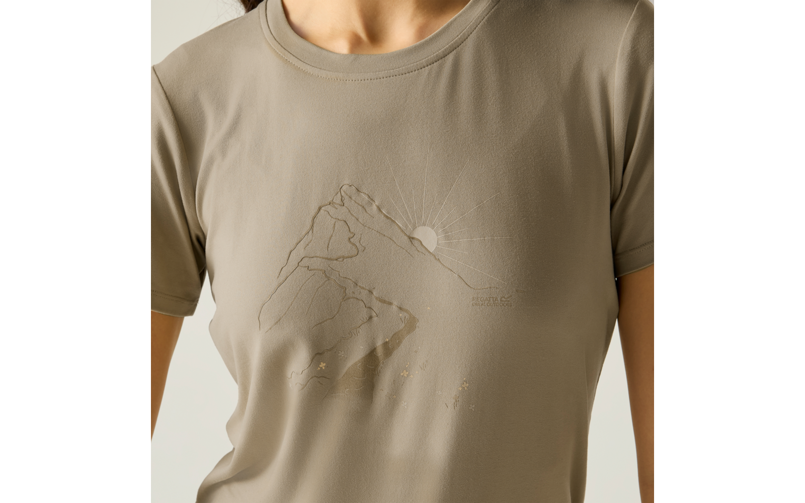 Nahaufnahme des Oberkörpers in einem beige T‑Shirt mit geprägt dargestelltem Berg, aufgehender Sonne und kleinen Sternen
