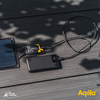 Eine Powerbank, die mit einem Solarpanel über ein Kabel verbunden ist, liegt auf einem Holztisch mit Schatten von Blättern